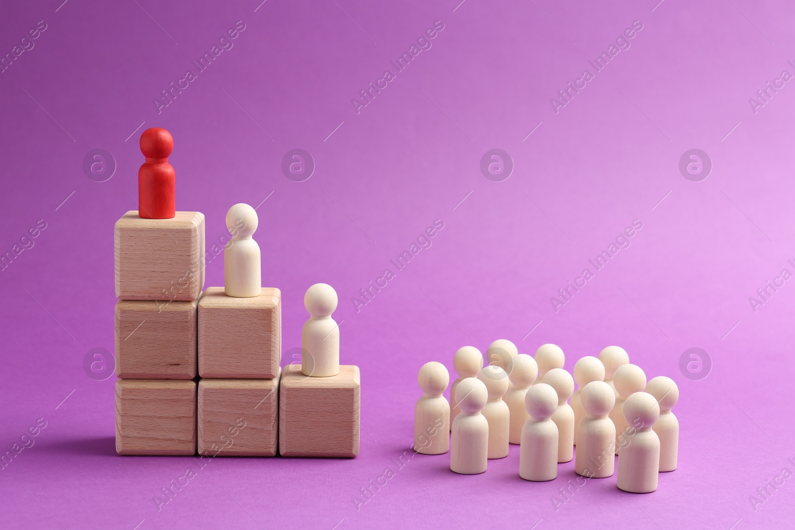 Photo of Human figures, red one on top of stacked wooden cubes against violet background. Competition concept