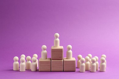 Photo of Human figures, wooden one on top of stacked cubes against violet background. Competition concept