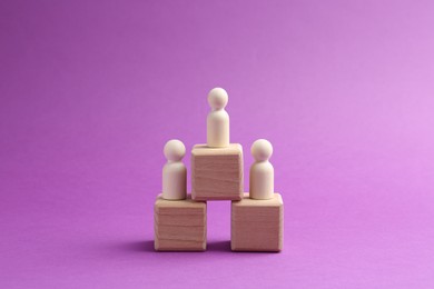 Photo of Human figures on cubes, wooden one on top against violet background. Competition concept