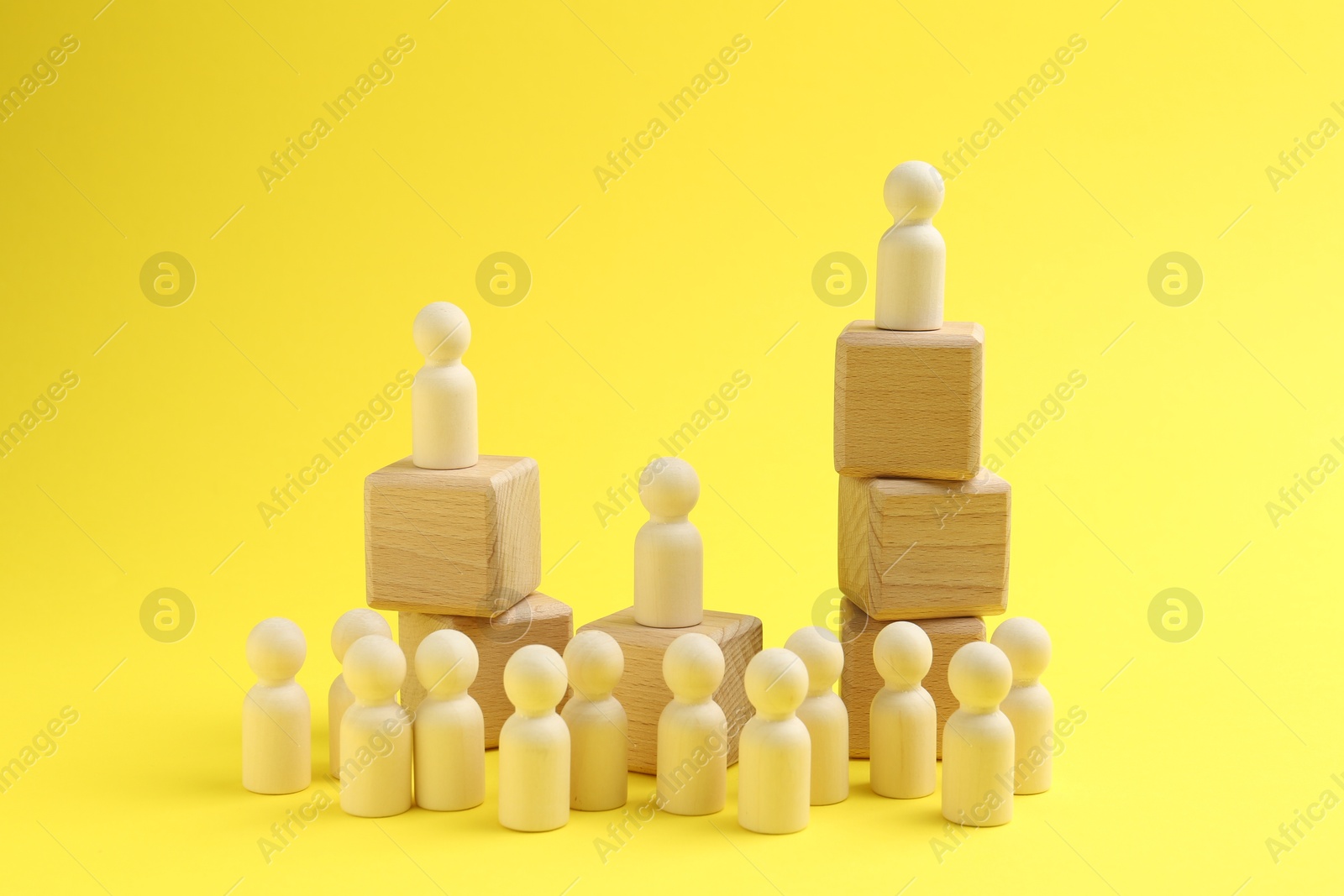 Photo of Human figures, wooden one on top of stacked cubes against yellow background. Competition concept