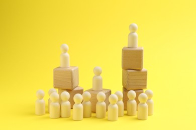 Photo of Human figures, wooden one on top of stacked cubes against yellow background. Competition concept