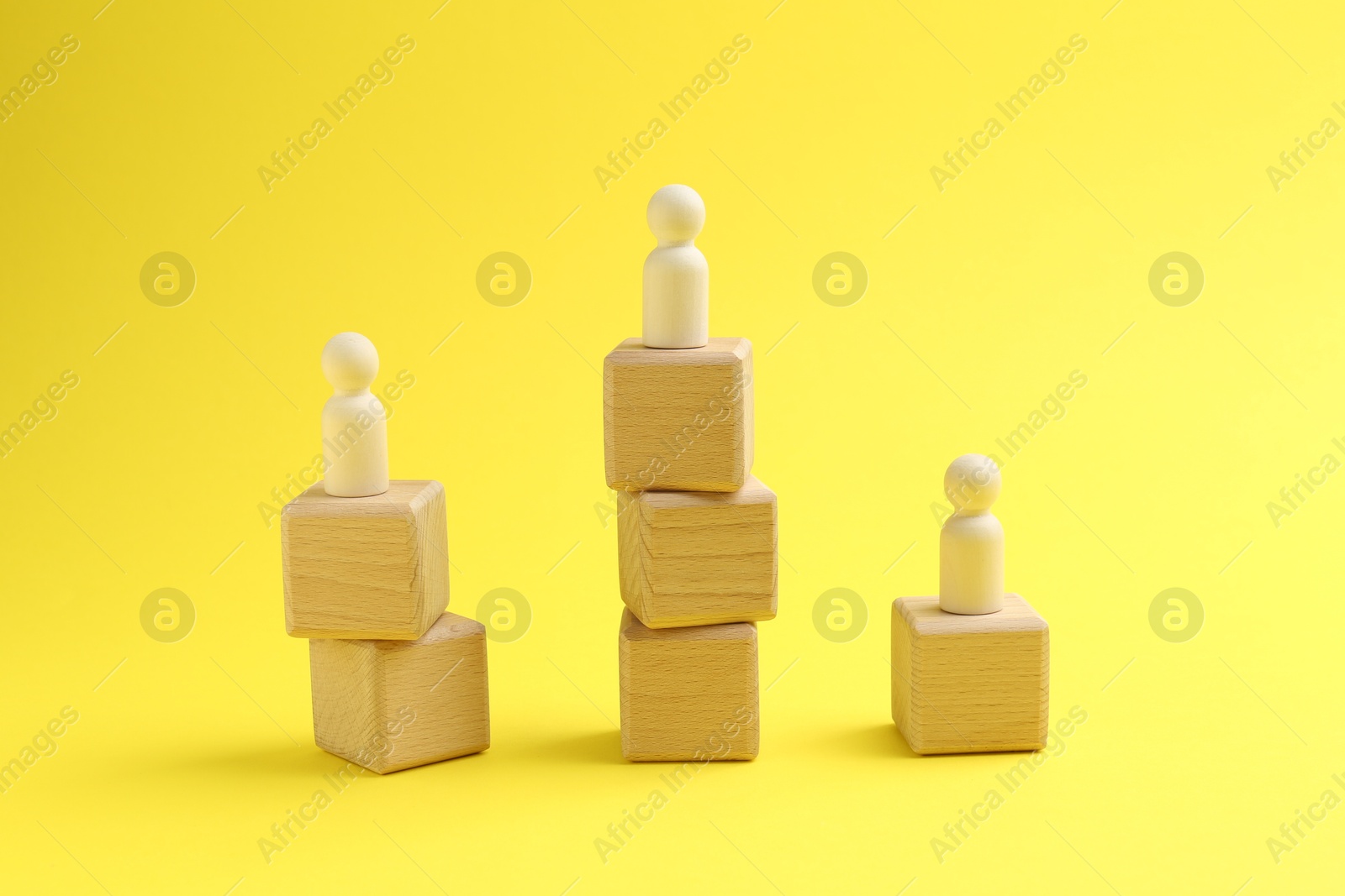 Photo of Human figures on stacked wooden cubes against yellow background. Competition concept