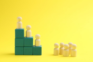 Photo of Wooden human figures on stacked cubes against yellow background. Competition concept