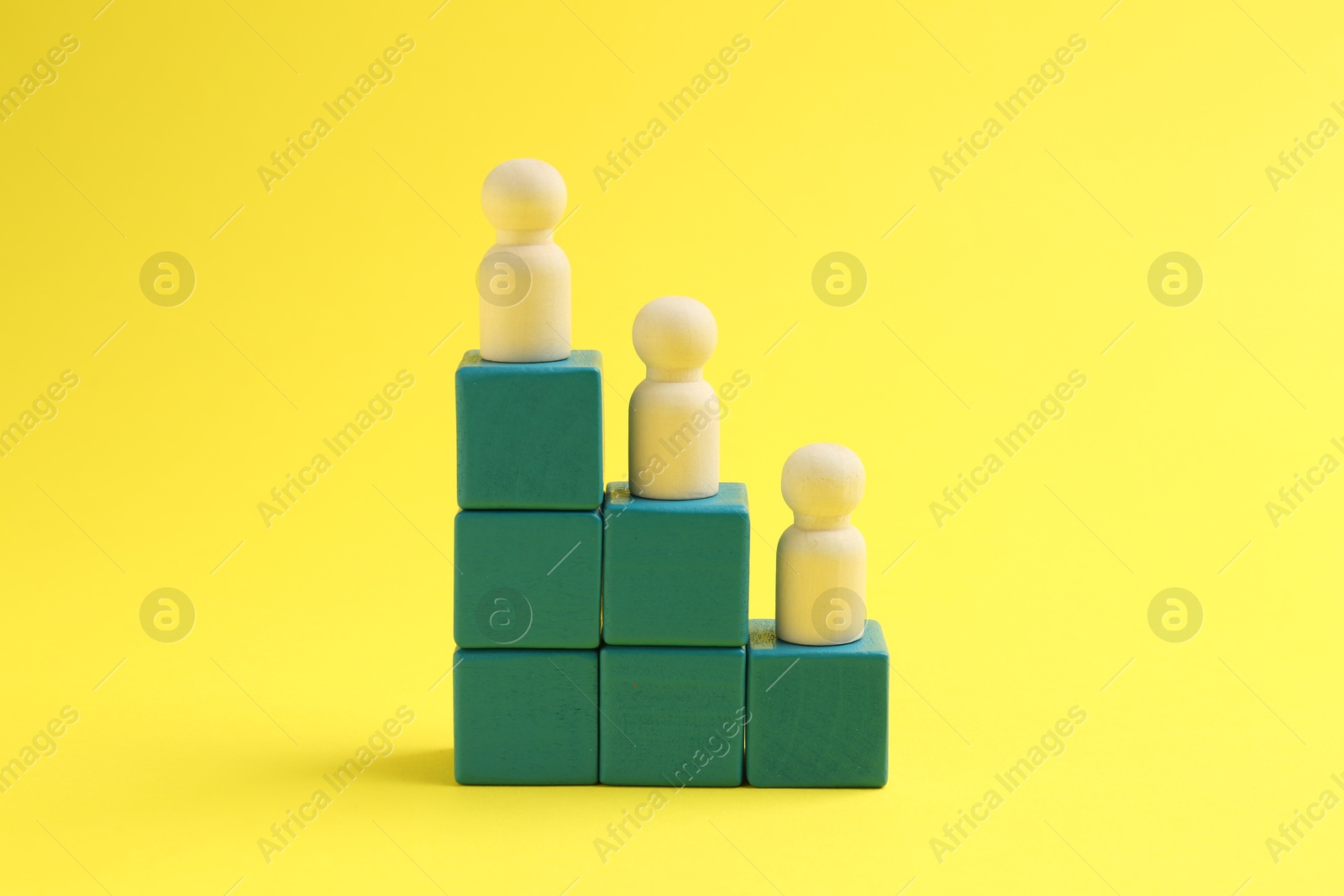 Photo of Human figures on stacked cubes against yellow background. Competition concept