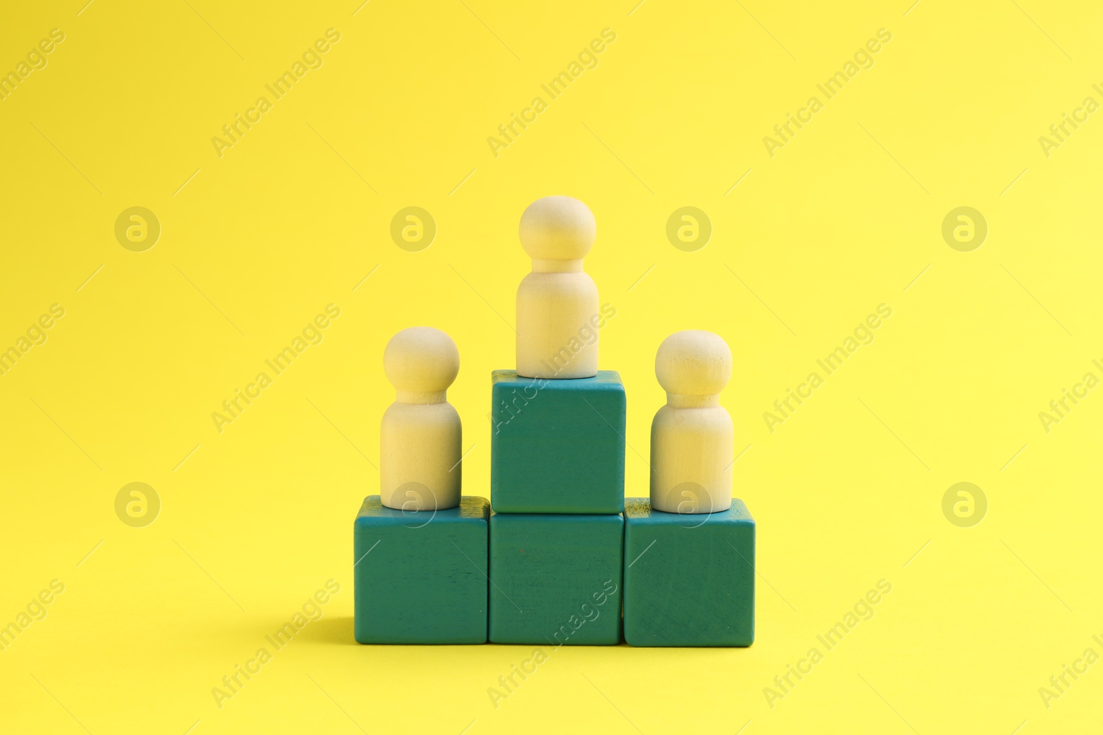 Photo of Human figures on green cubes, wooden one on top against yellow background. Competition concept