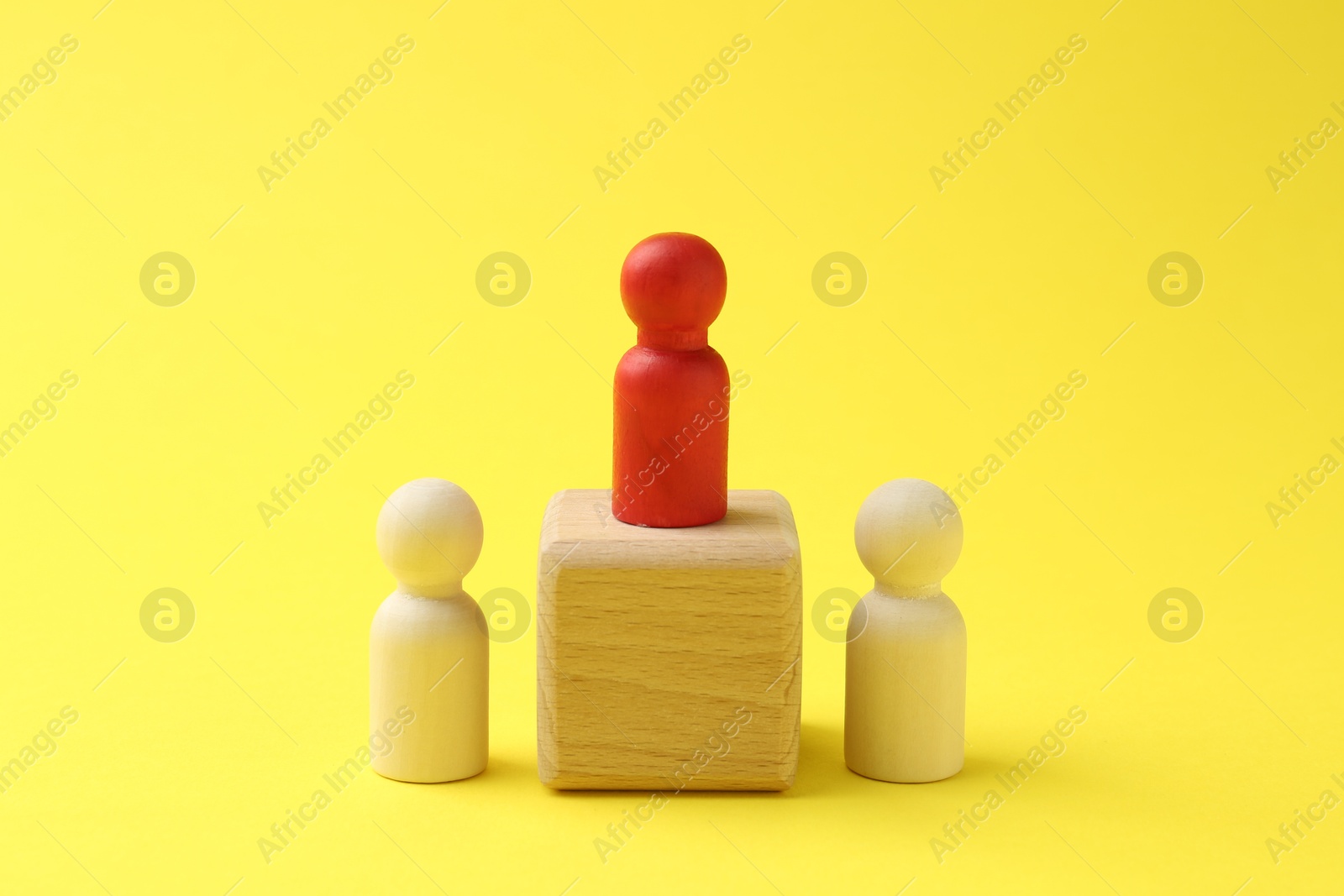 Photo of Human figures, red one on wooden cube against yellow background. Competition concept