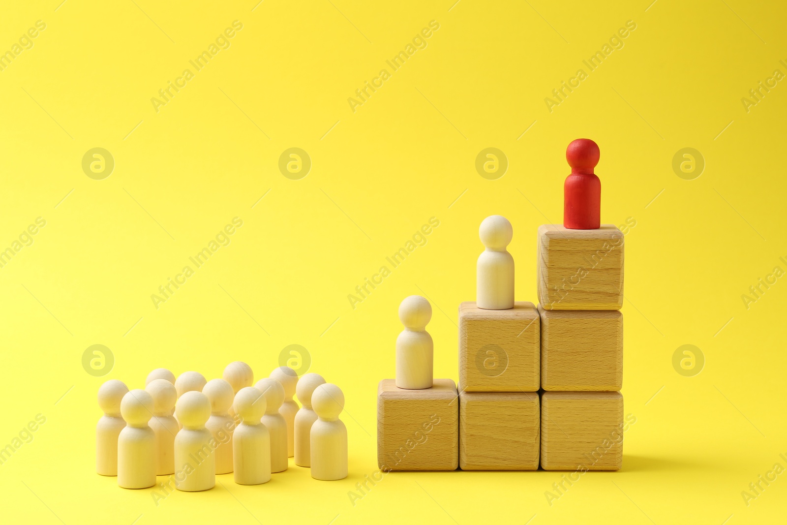 Photo of Human figures, red one on top of stacked wooden cubes against yellow background. Competition concept