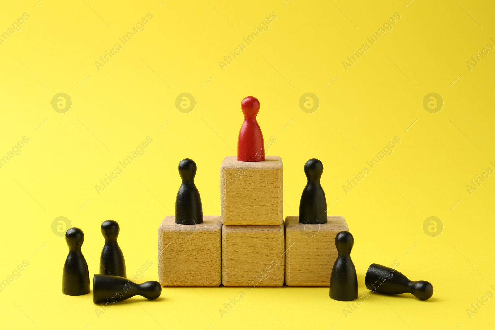 Photo of Human figures, red one on top of stacked wooden cubes against yellow background. Competition concept