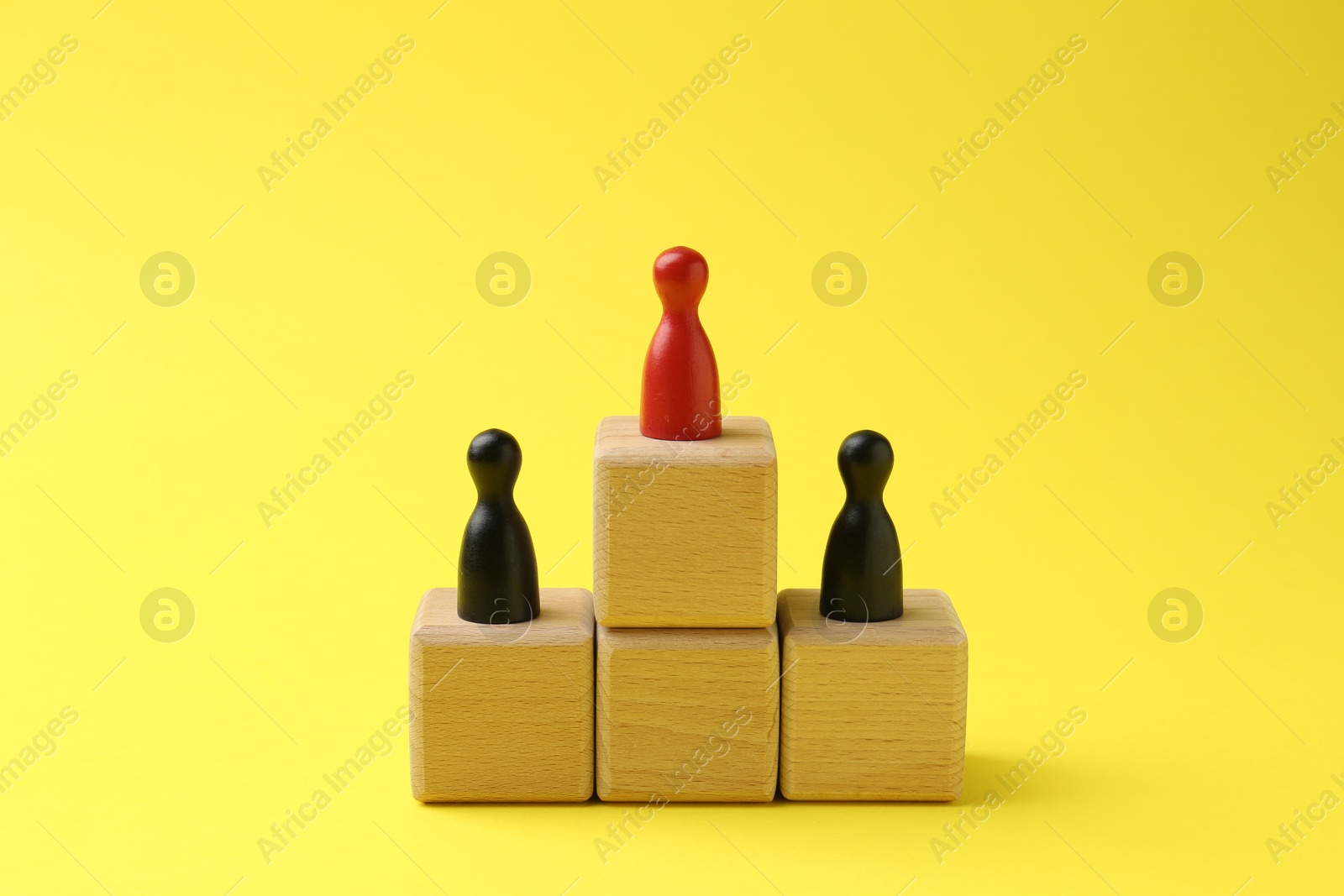 Photo of Human figures on wooden cubes, red one on top against yellow background. Competition concept