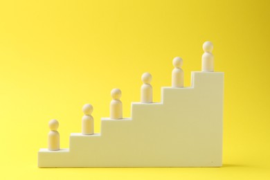 Photo of Human figures on stairs against yellow background. Competition concept