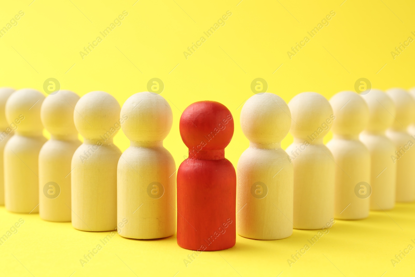 Photo of Red human figure among wooden ones against yellow background, closeup. Competition concept