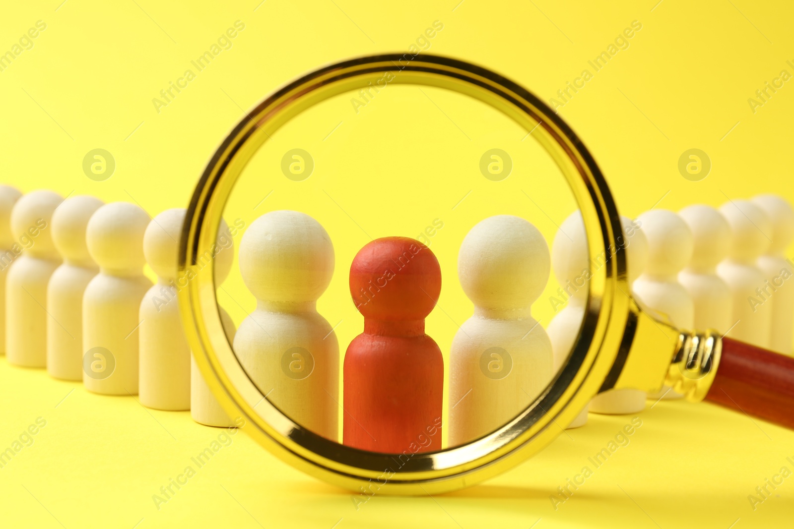 Photo of Looking at human figures through magnifying glass against yellow background, closeup. Competition concept