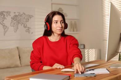 Photo of Woman with headphones working on computer at desk in home office