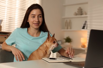 Photo of Young woman with her cute dog working on laptop at desk in home office