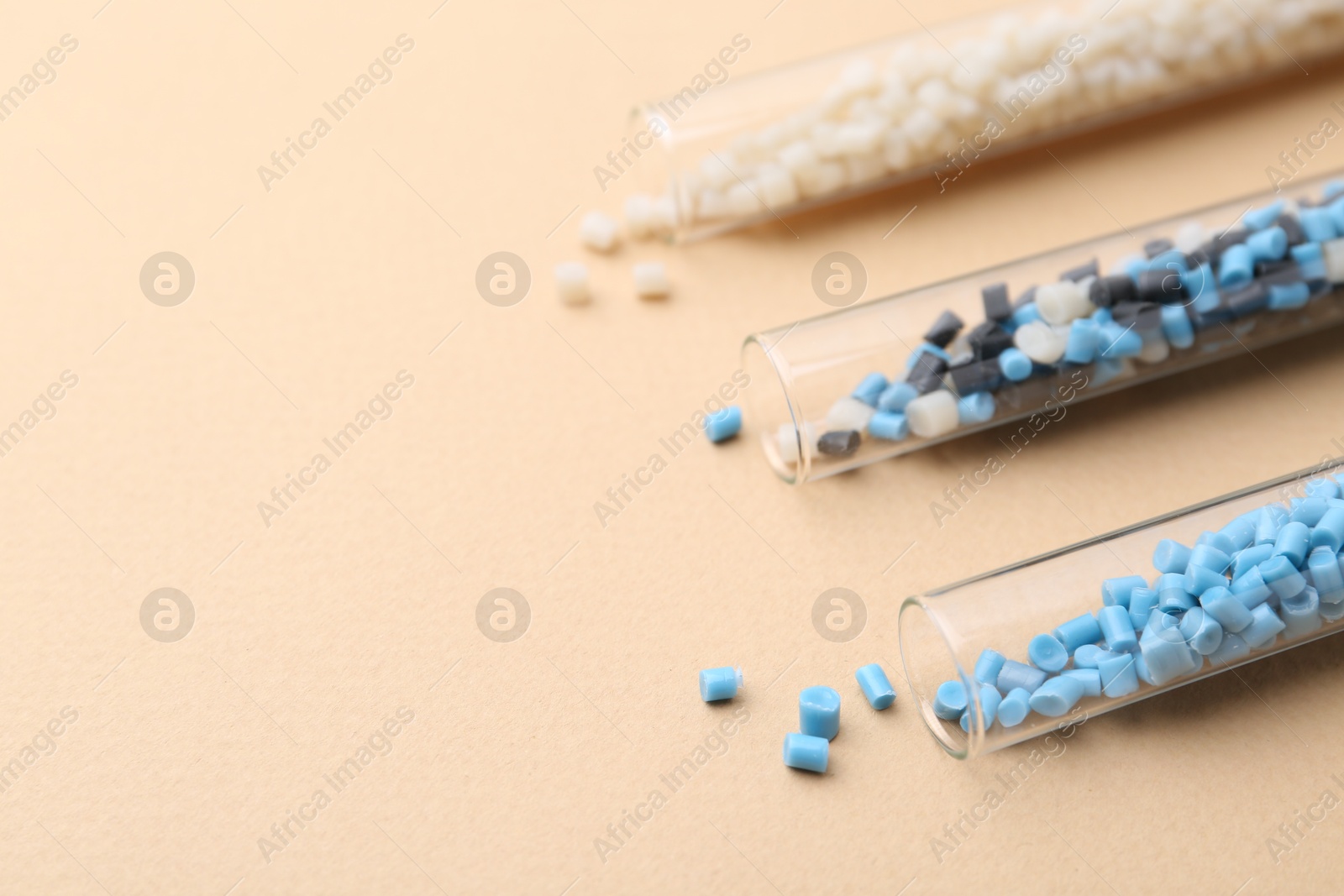 Photo of Colorful plastic granules in test tubes on beige background, closeup. Space for text