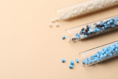 Colorful plastic granules in test tubes on beige background, closeup. Space for text