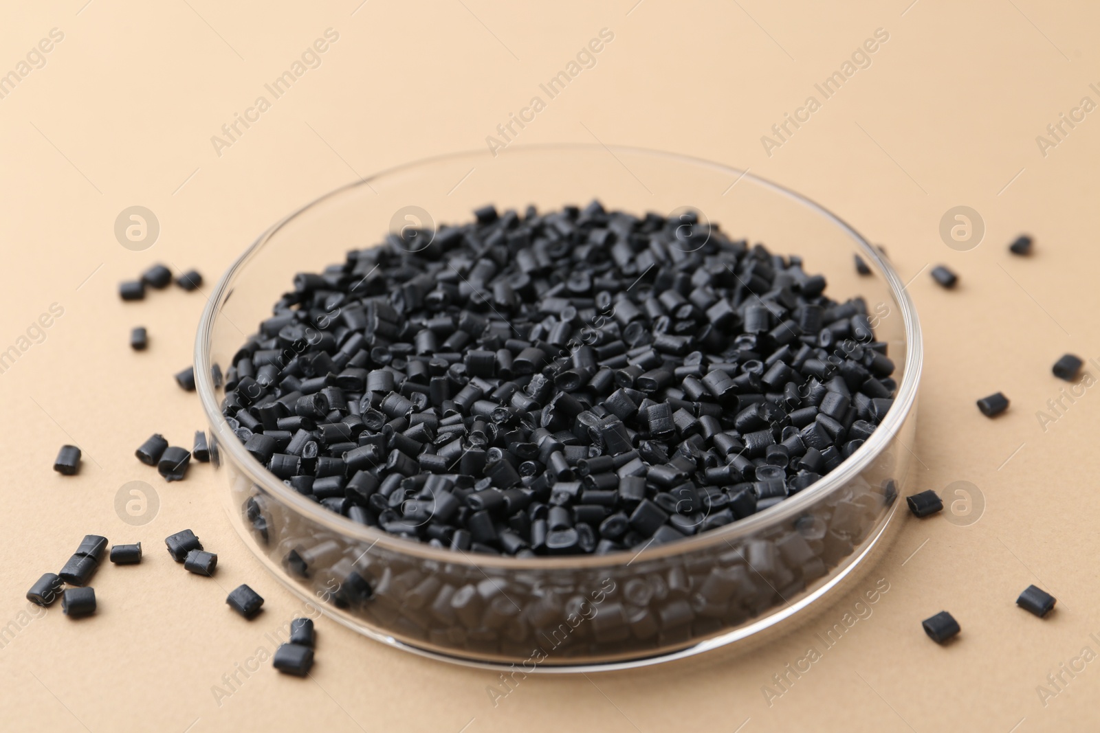 Photo of Black plastic granules in petri dish on beige background, closeup