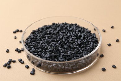 Photo of Black plastic granules in petri dish on beige background, closeup