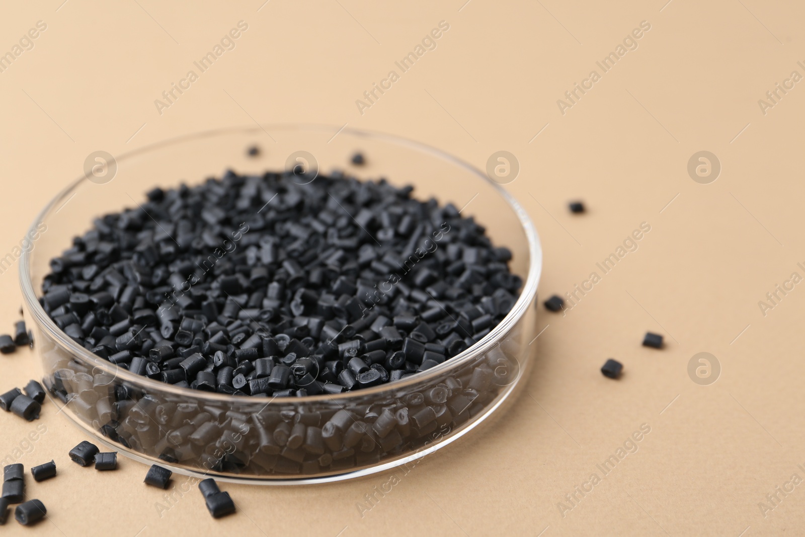 Photo of Black plastic granules in petri dish on beige background, closeup. Space for text