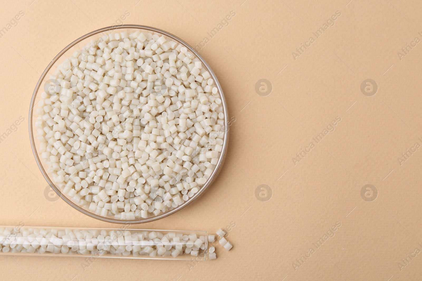 Photo of Plastic granules in petri dish and test tube on beige background, flat lay. Space for text