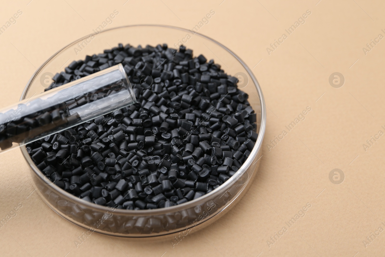 Photo of Black plastic granules in petri dish and test tube on beige background, closeup. Space for text