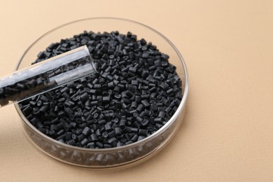 Black plastic granules in petri dish and test tube on beige background, closeup. Space for text