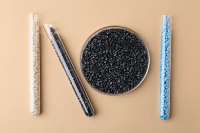 Colorful plastic granules in petri dish and test tubes on beige background, flat lay