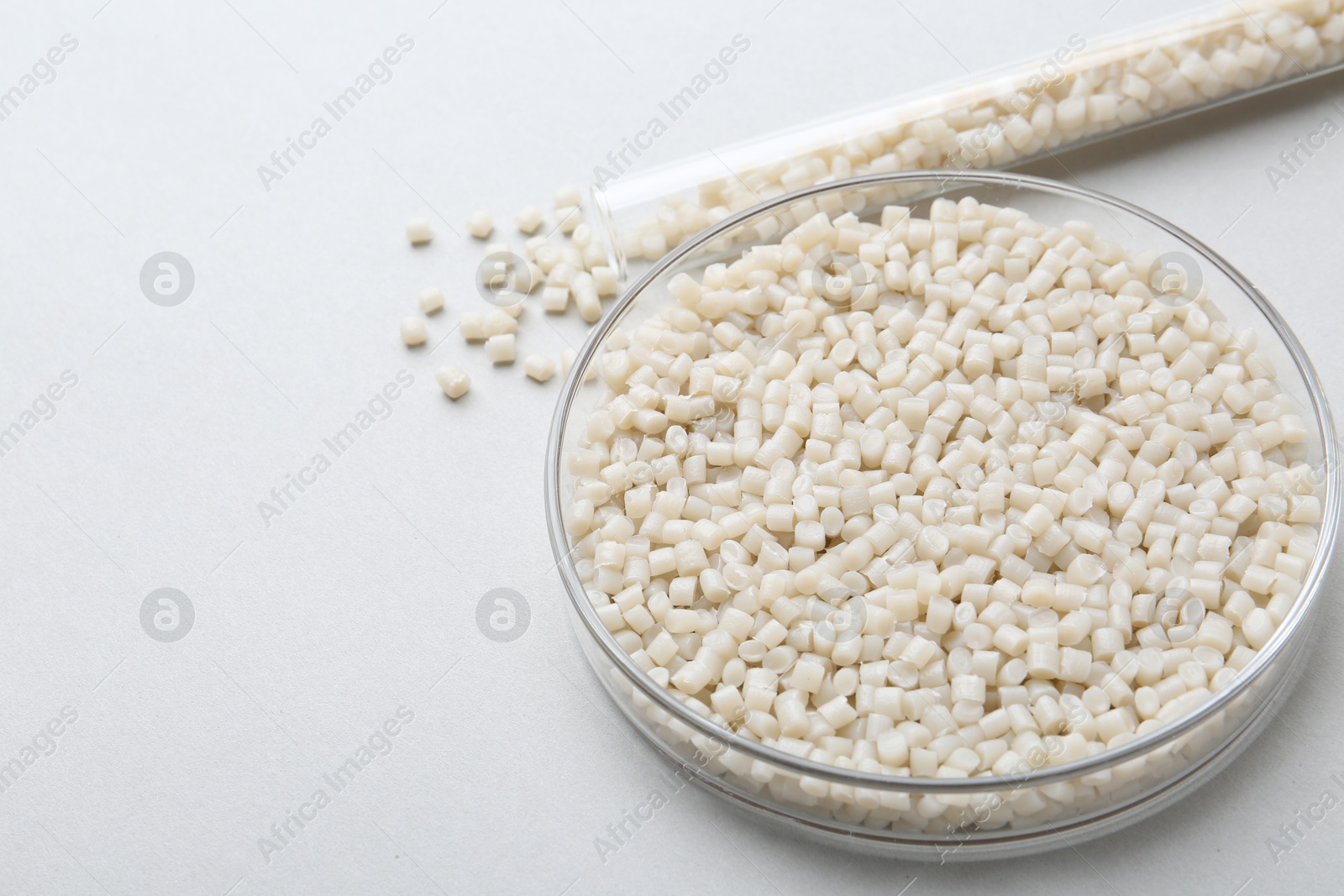 Photo of Plastic granules in petri dish and test tube on gray background, closeup. Space for text