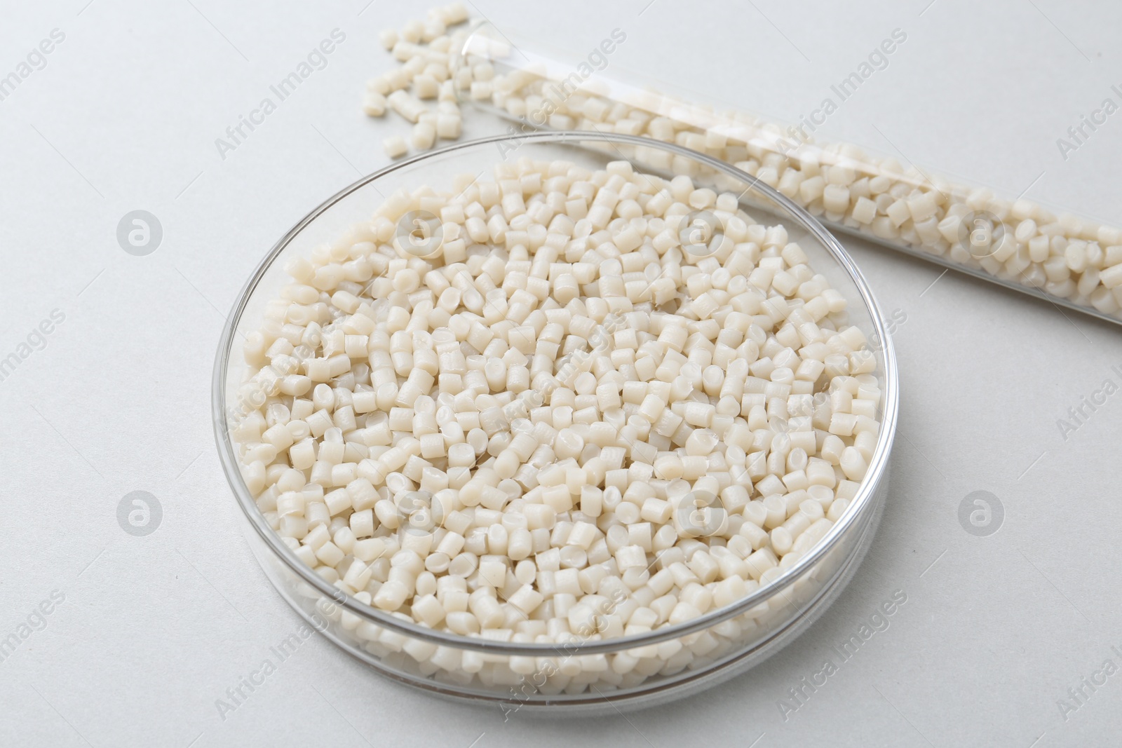 Photo of Plastic granules in petri dish and test tube on gray background, closeup