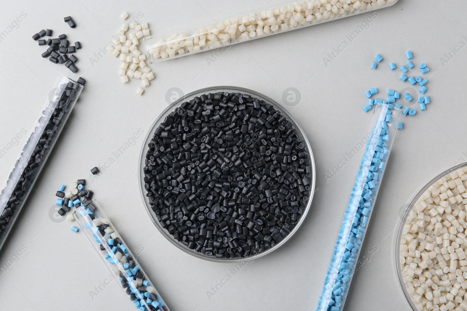 Photo of Colorful plastic granules in petri dish and test tubes on gray background, flat lay