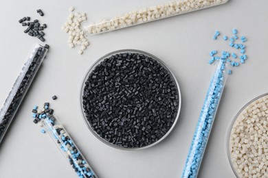 Colorful plastic granules in petri dish and test tubes on gray background, flat lay