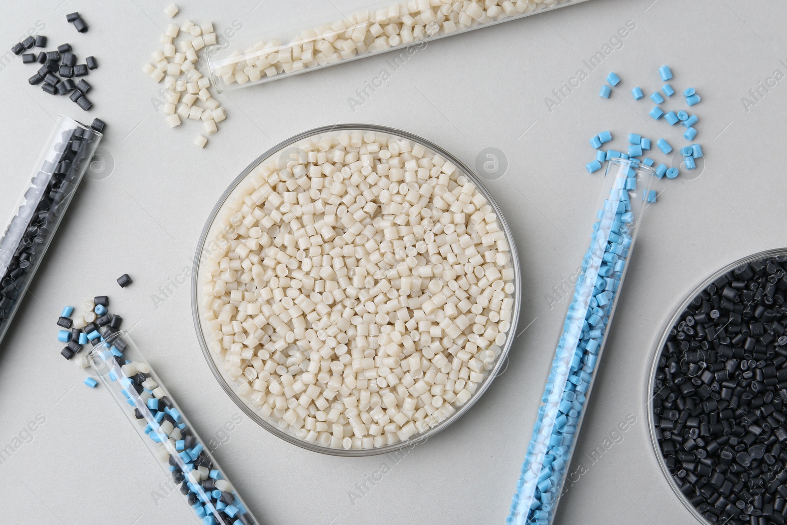 Photo of Colorful plastic granules in petri dish and test tubes on gray background, flat lay