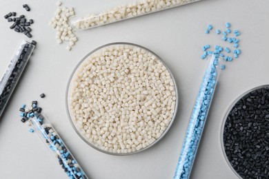 Colorful plastic granules in petri dish and test tubes on gray background, flat lay