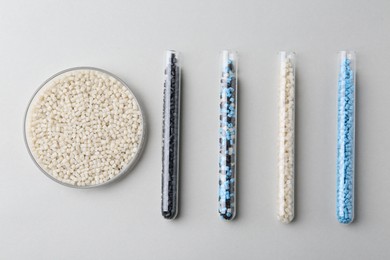 Colorful plastic granules in petri dish and test tubes on gray background, flat lay