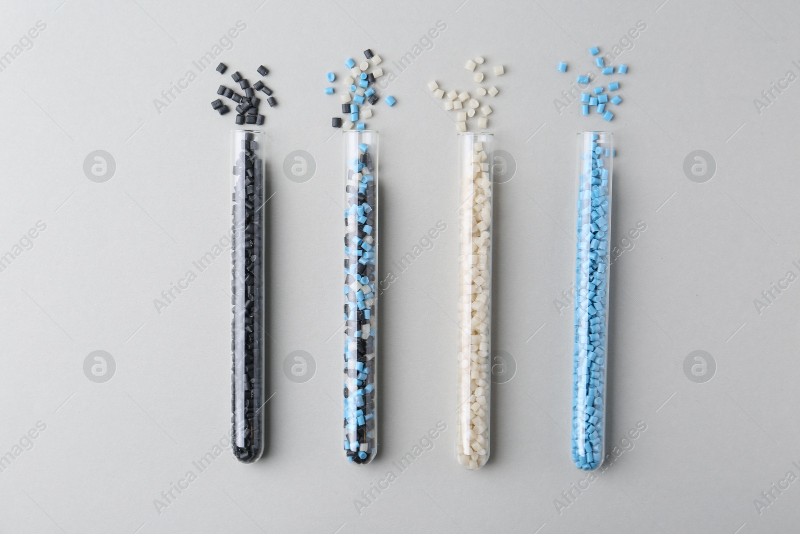 Photo of Colorful plastic granules in test tubes on gray background, flat lay