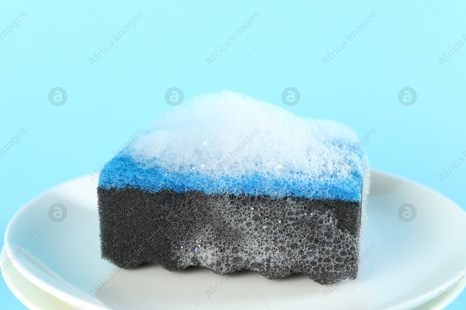 Photo of Sponge with foam and plates on light blue background, closeup