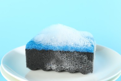 Photo of Sponge with foam and plates on light blue background, closeup