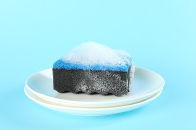 Photo of Sponge with foam and plates on light blue background, closeup