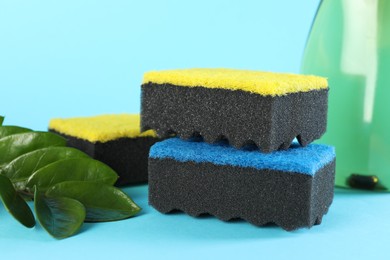 Photo of Many colorful sponges and branch with leaves on light blue background, closeup