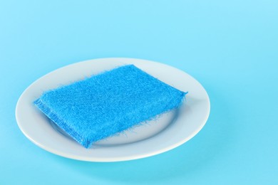 Photo of Sponge and plate on light blue background, closeup. Space for text