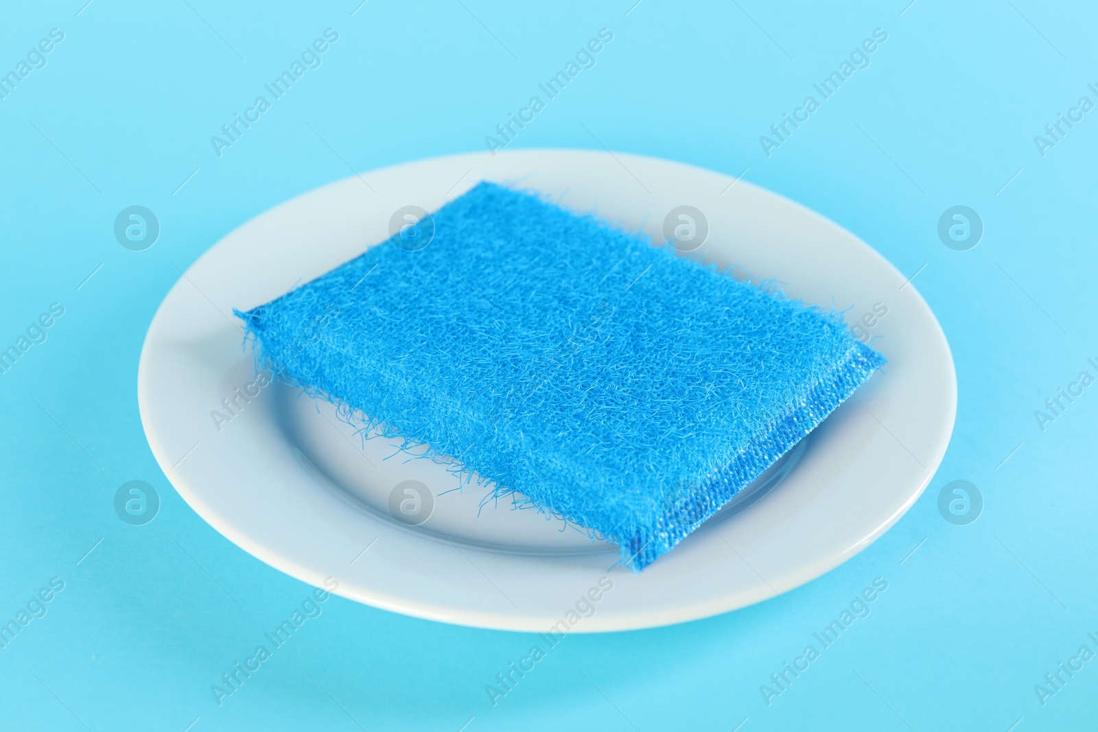 Photo of Sponge and plate on light blue background, closeup