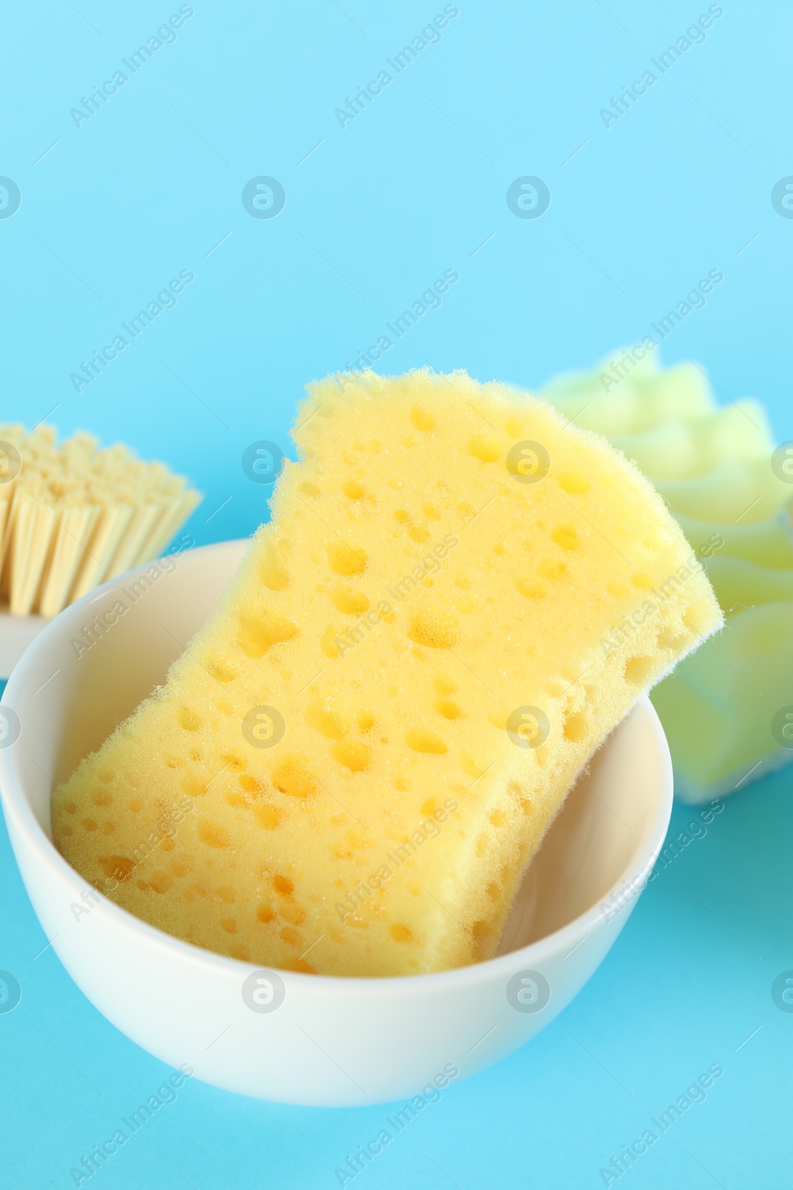 Photo of Sponges and bowl on light blue background, closeup