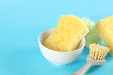 Photo of Sponges, bowl and brush on light blue background, closeup. Space for text