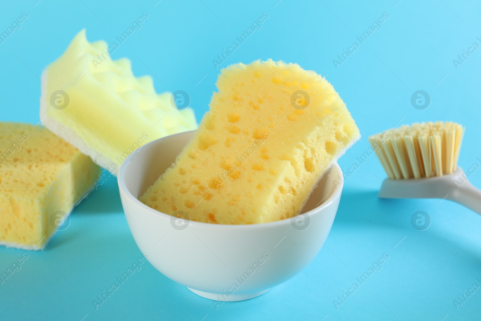 Photo of Sponges, bowl and brush on light blue background, closeup