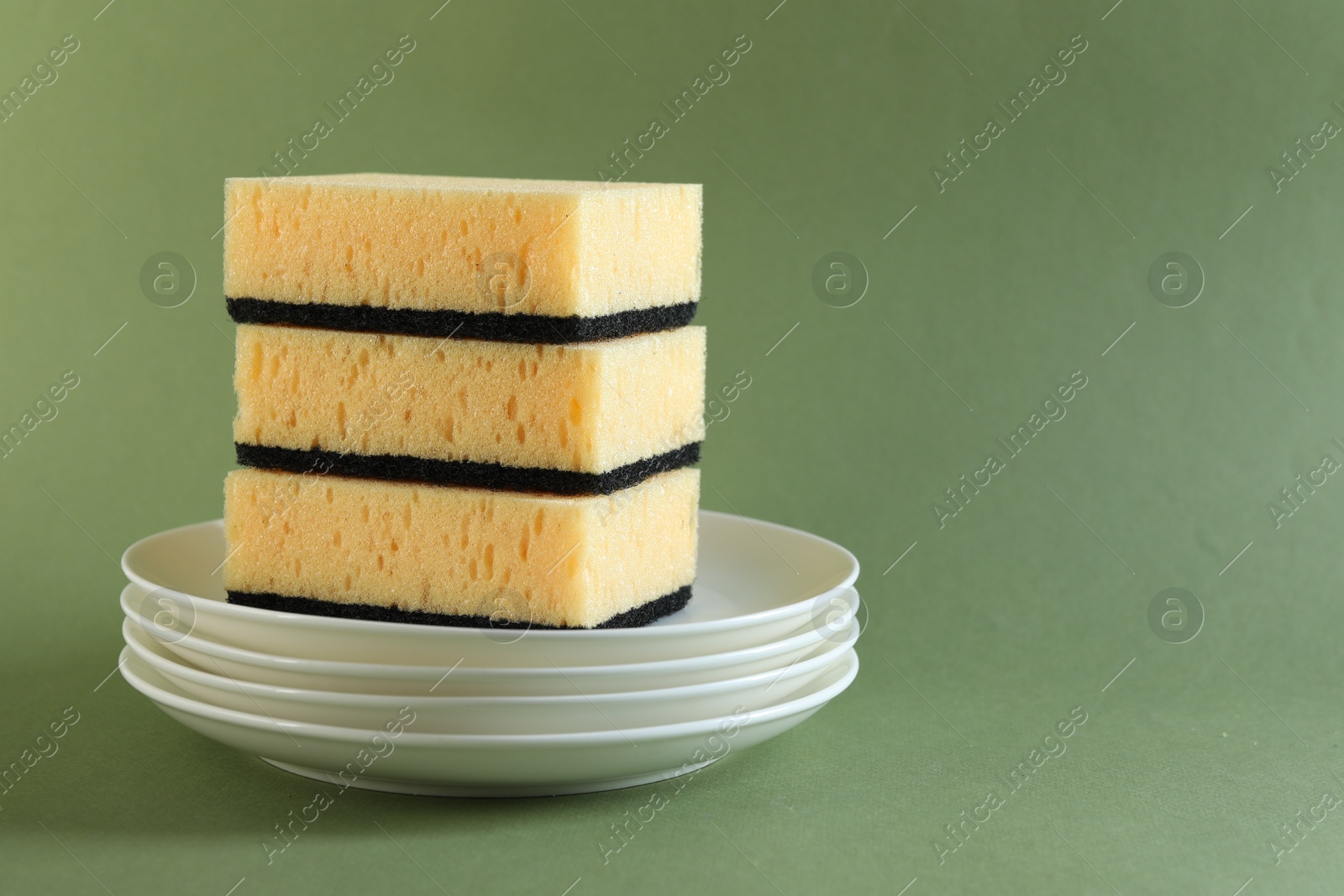 Photo of Stack of sponges and clean plates on green background, closeup. Space for text