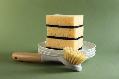 Photo of Stack of sponges, clean plates and brush on green background, closeup