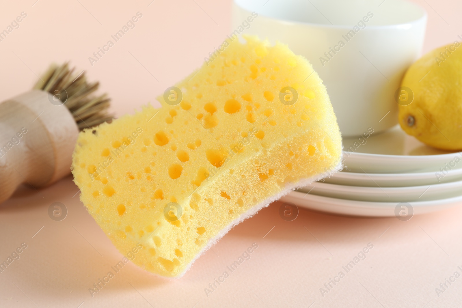 Photo of Sponge, dishware, lemon and brush on beige background, closeup