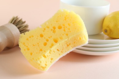 Photo of Sponge, dishware, lemon and brush on beige background, closeup