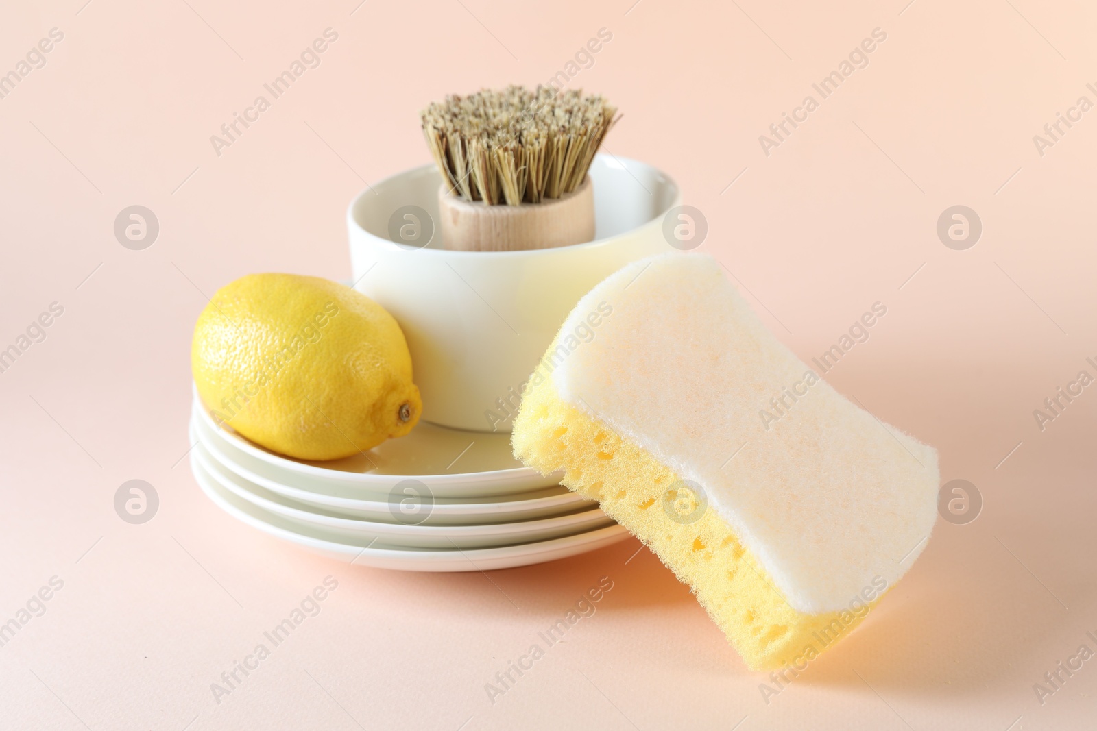 Photo of Sponge, dishware, lemon and brush on beige background, closeup