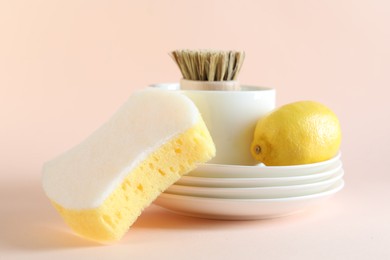 Photo of Sponge, dishware, lemon and brush on beige background, closeup